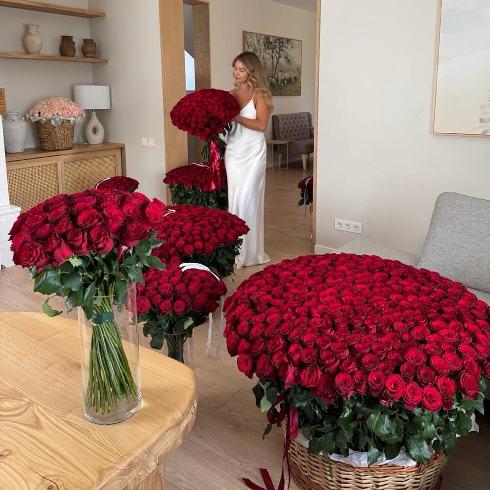Woman in a white dress standing in a room with large arrangements of 1000 red roses.