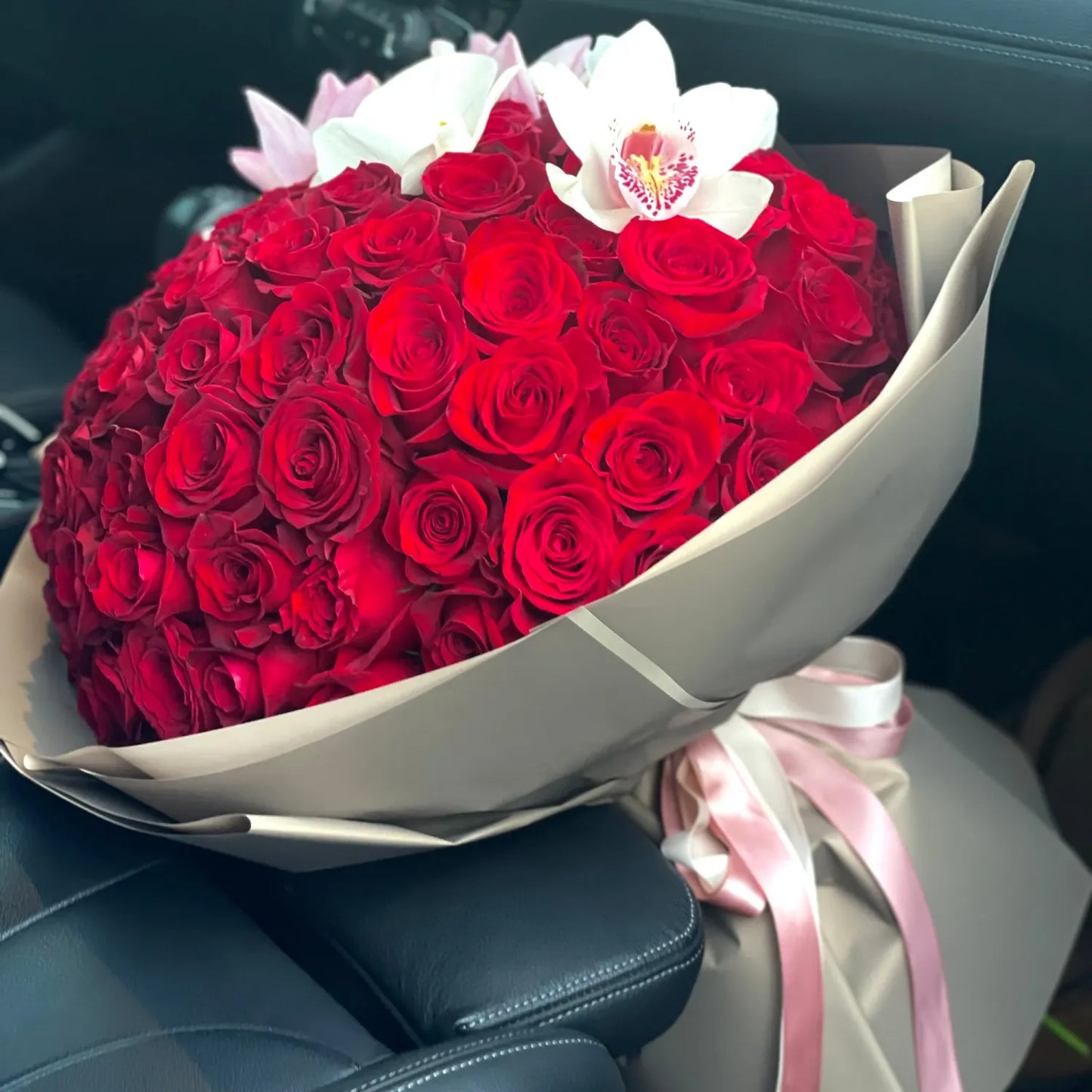 Bouquet of 100 red roses with a pink ribbon on a car seat